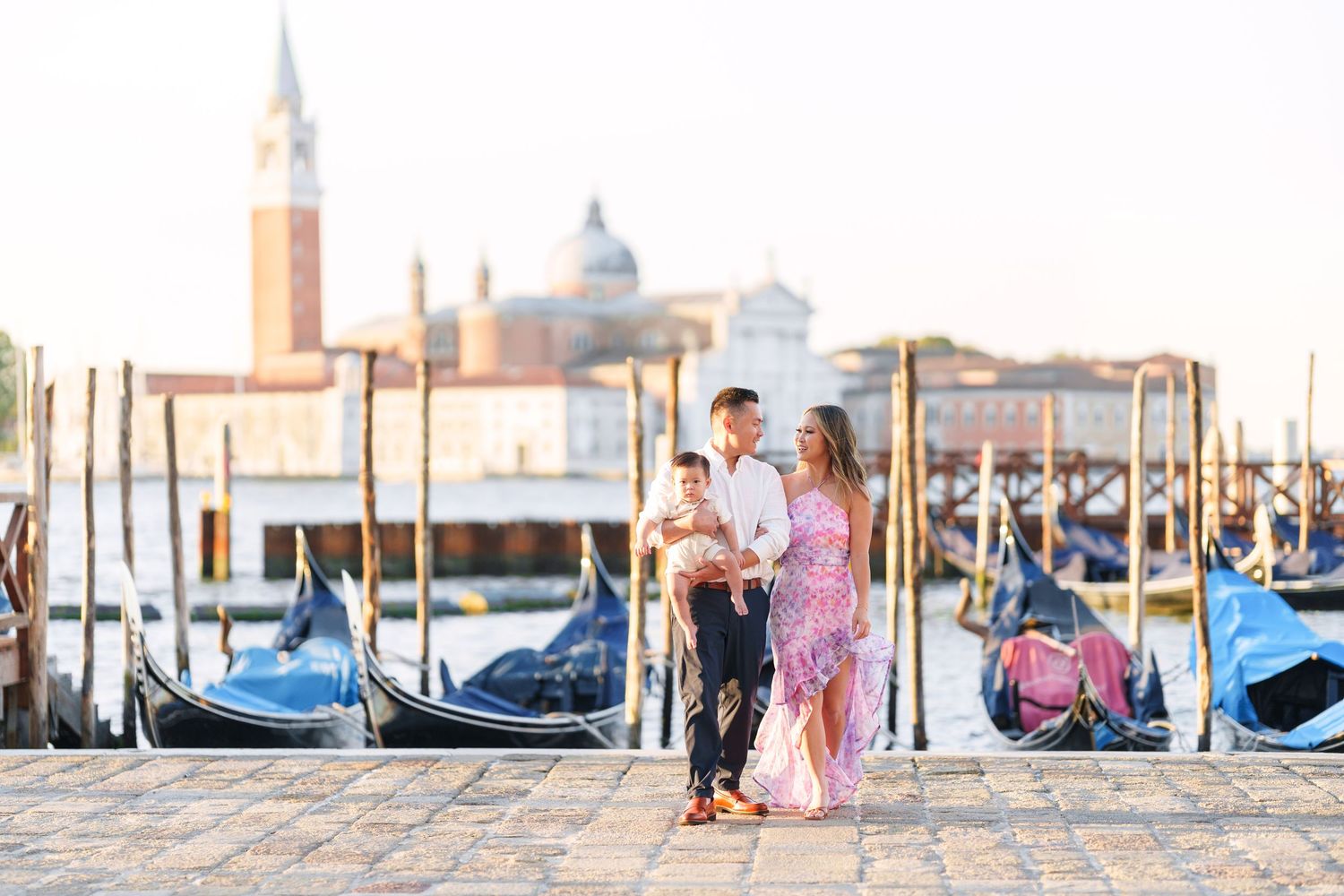 Couple with a child enjoying a romantic sunset walk along Venice waterfront with gondolas.
