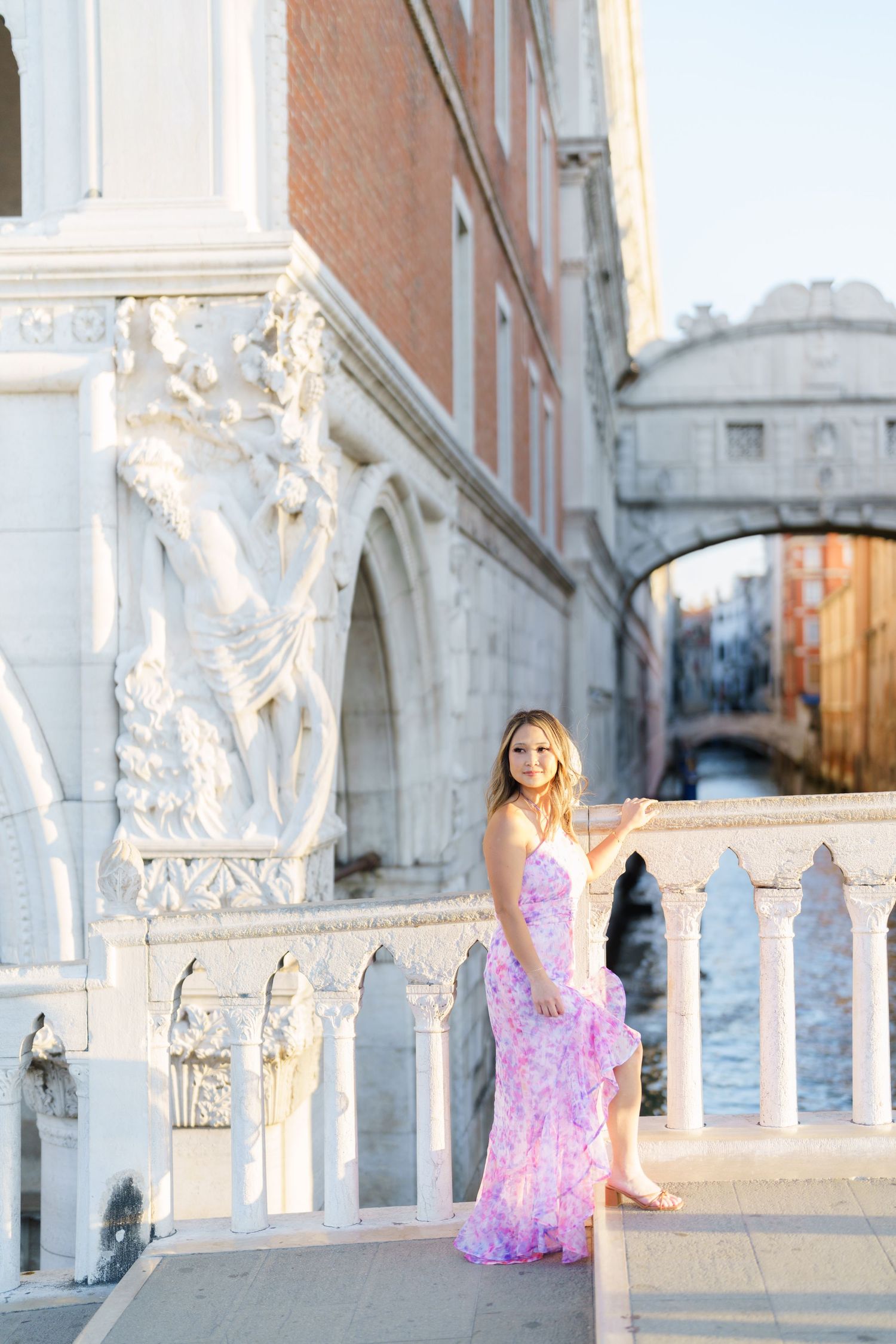 Woman in pink floral dress posing near the Bridge of Sighs in Venice, Italy on a sunny day.