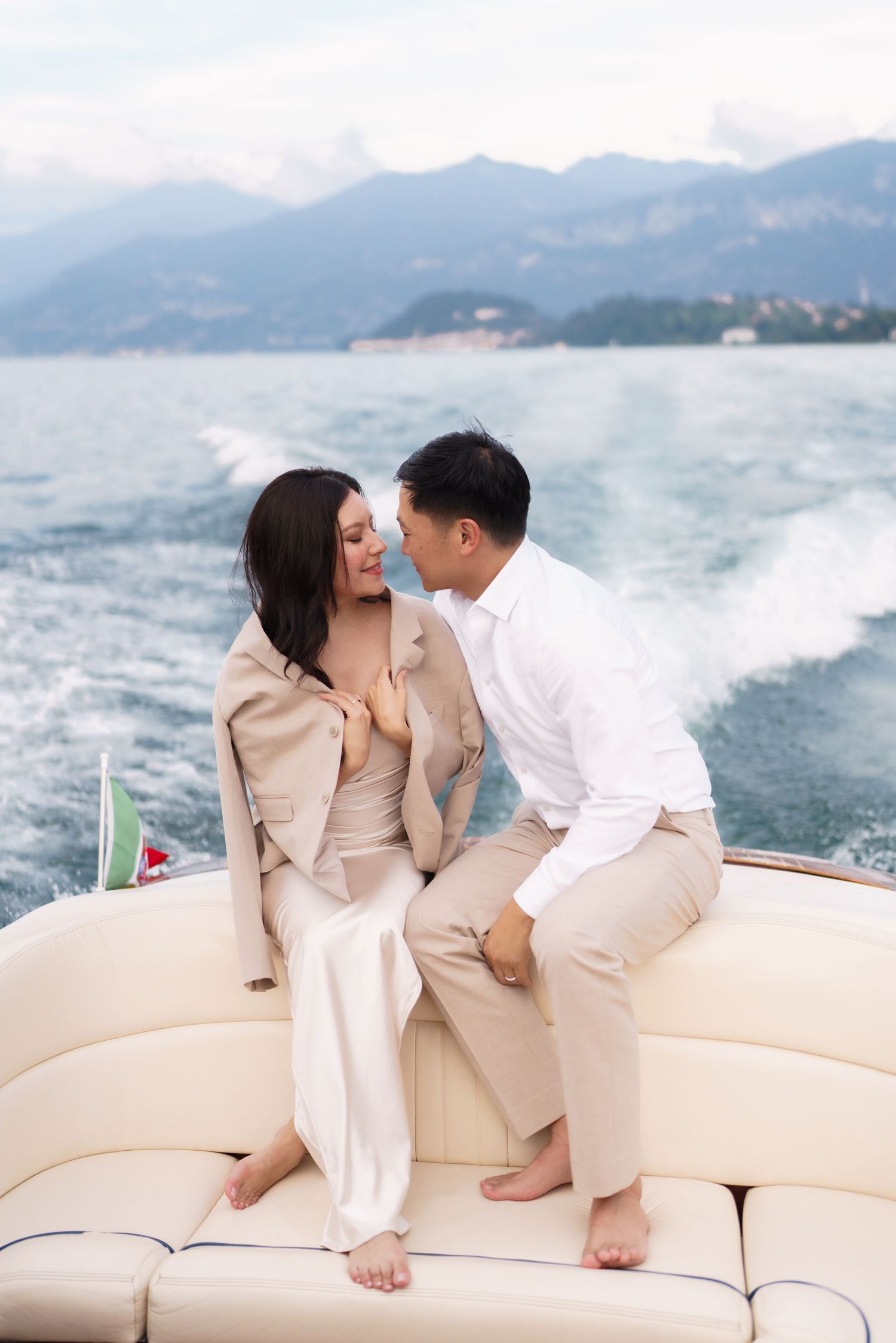 A couple shares an intimate moment on a boat with misty mountains and ocean waves in the background.