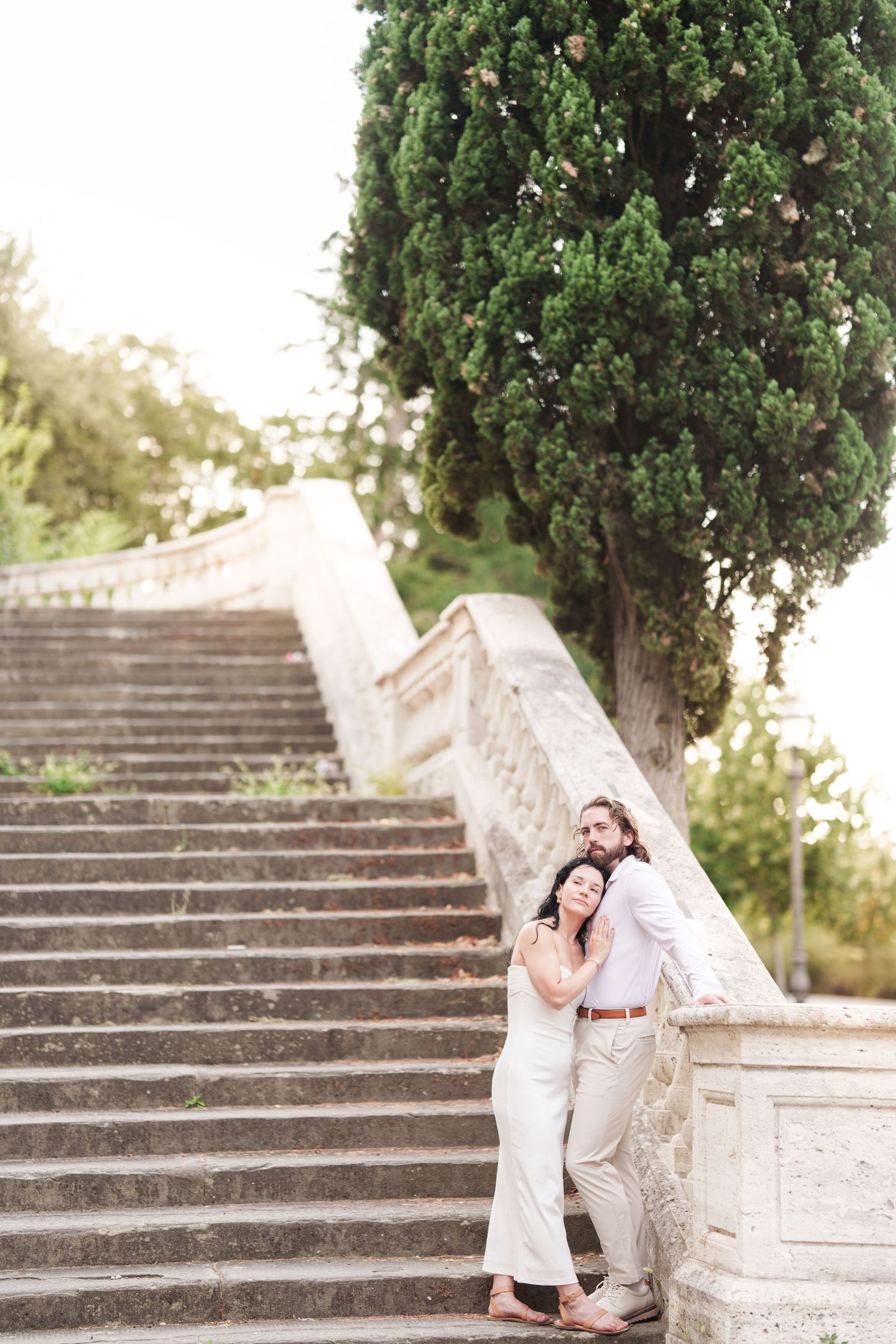 A romantic couple poses on stone steps surrounded by lush greenery in an outdoor garden setting.