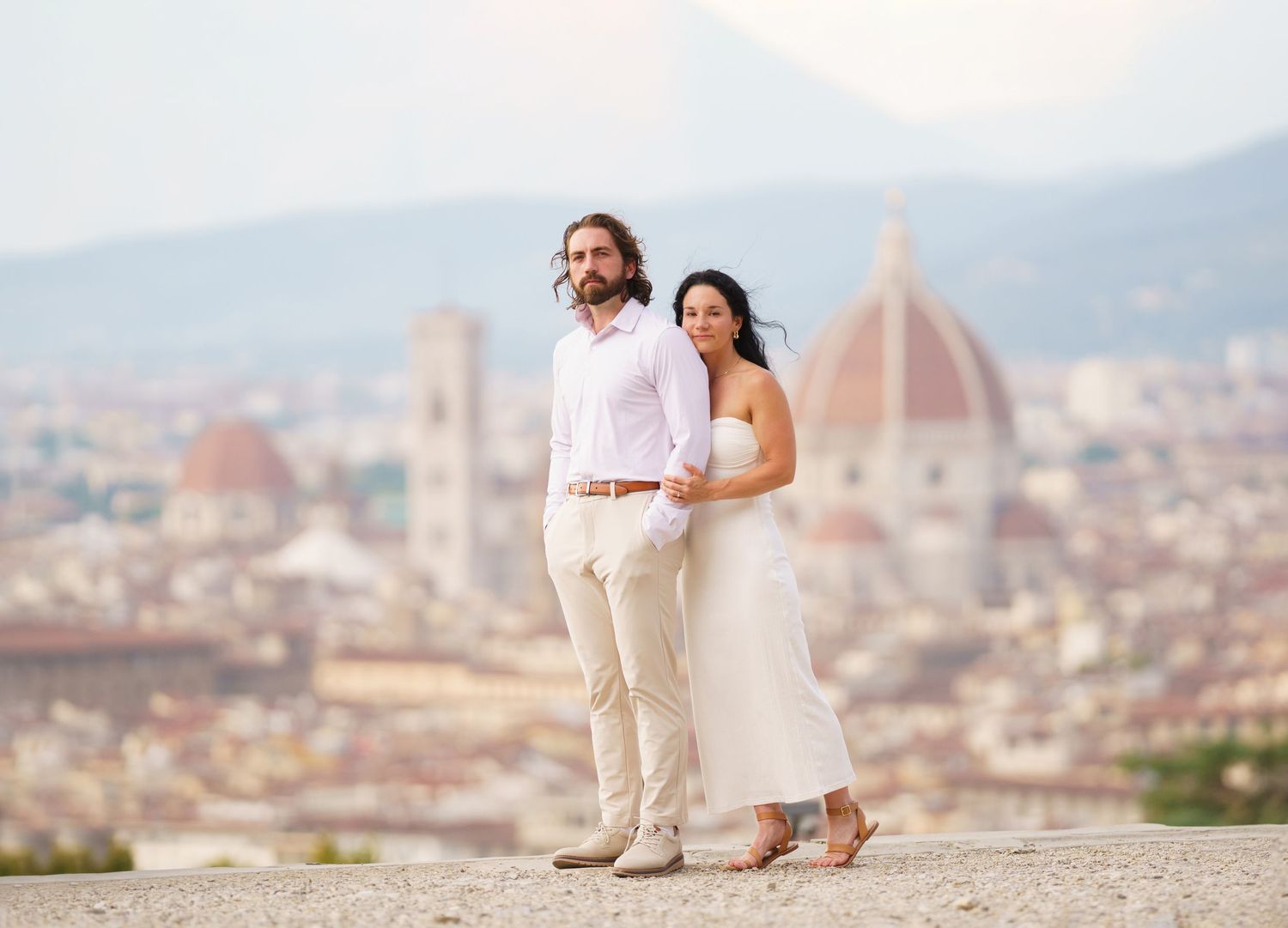 Couple sitting together on stone wall overlooking panoramic view of Florence with historic architecture.