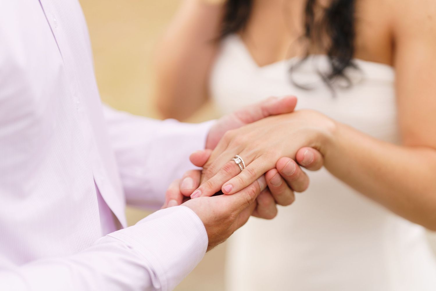 Close up view of two hands clasped together in a tender moment during a wedding ceremony.