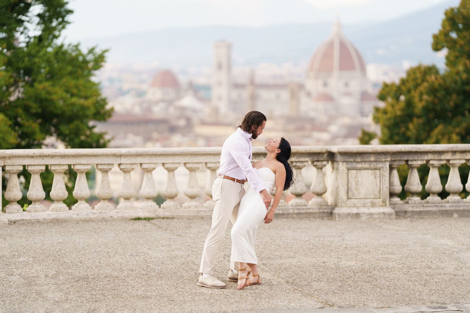 A romantic couple in white outfits poses for wedding photos with Florence's iconic Duomo cathedral in the background.
