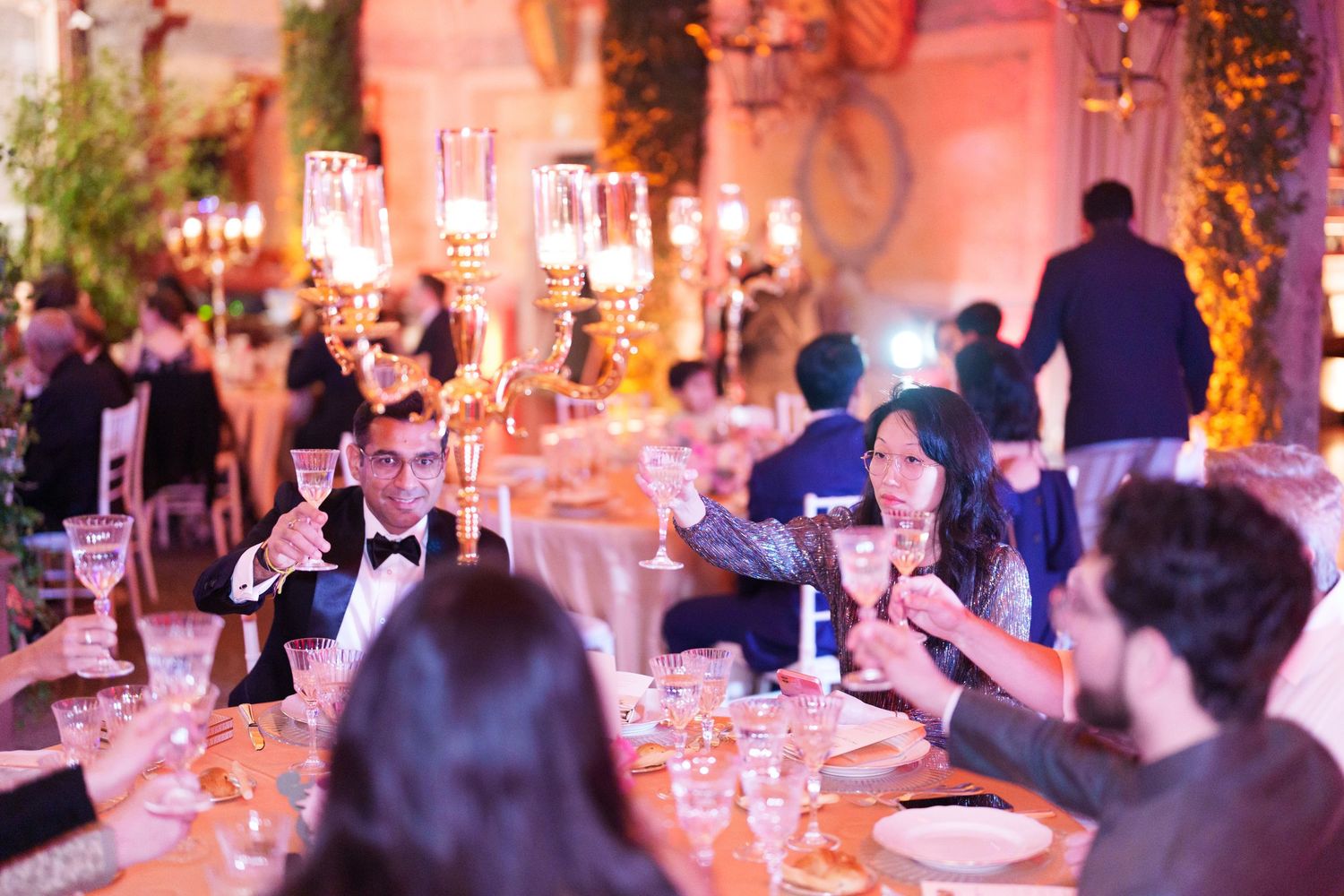 Elegant wedding reception dinner with candlelit tables and dramatic pink lighting effects.