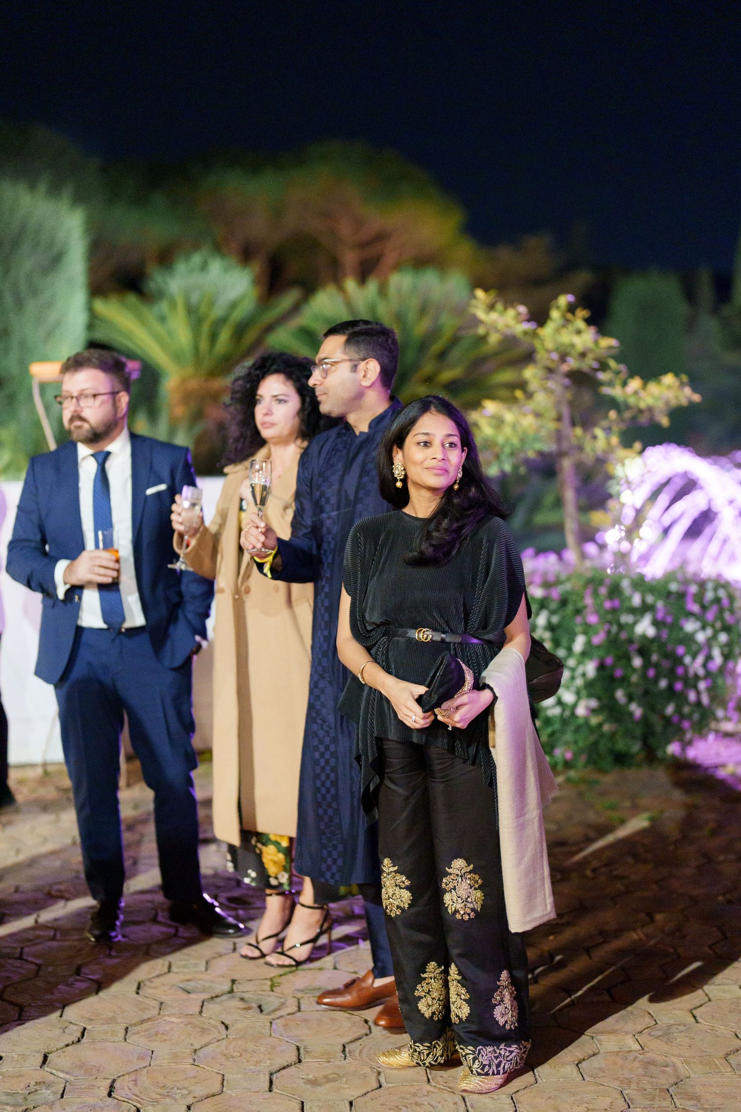 Formal evening gathering with guests in elegant attire at an outdoor garden venue.