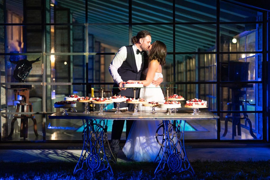 Romantic evening dessert table with ornate base illuminated by blue lighting at wedding reception.
