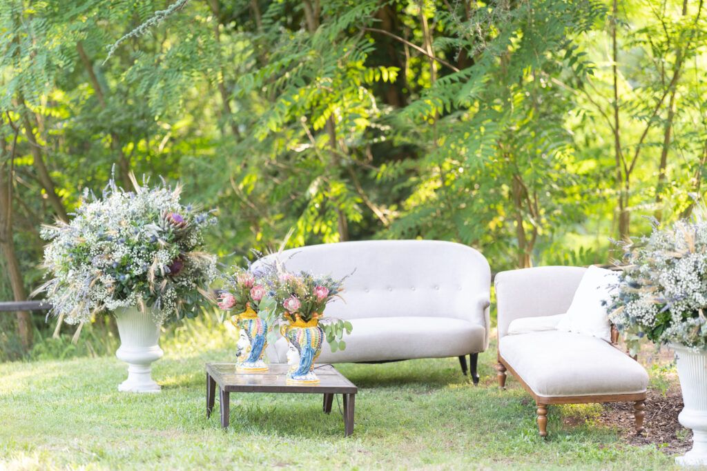 Garden seating area with plush white cushions and floral arrangements in a natural outdoor setting.