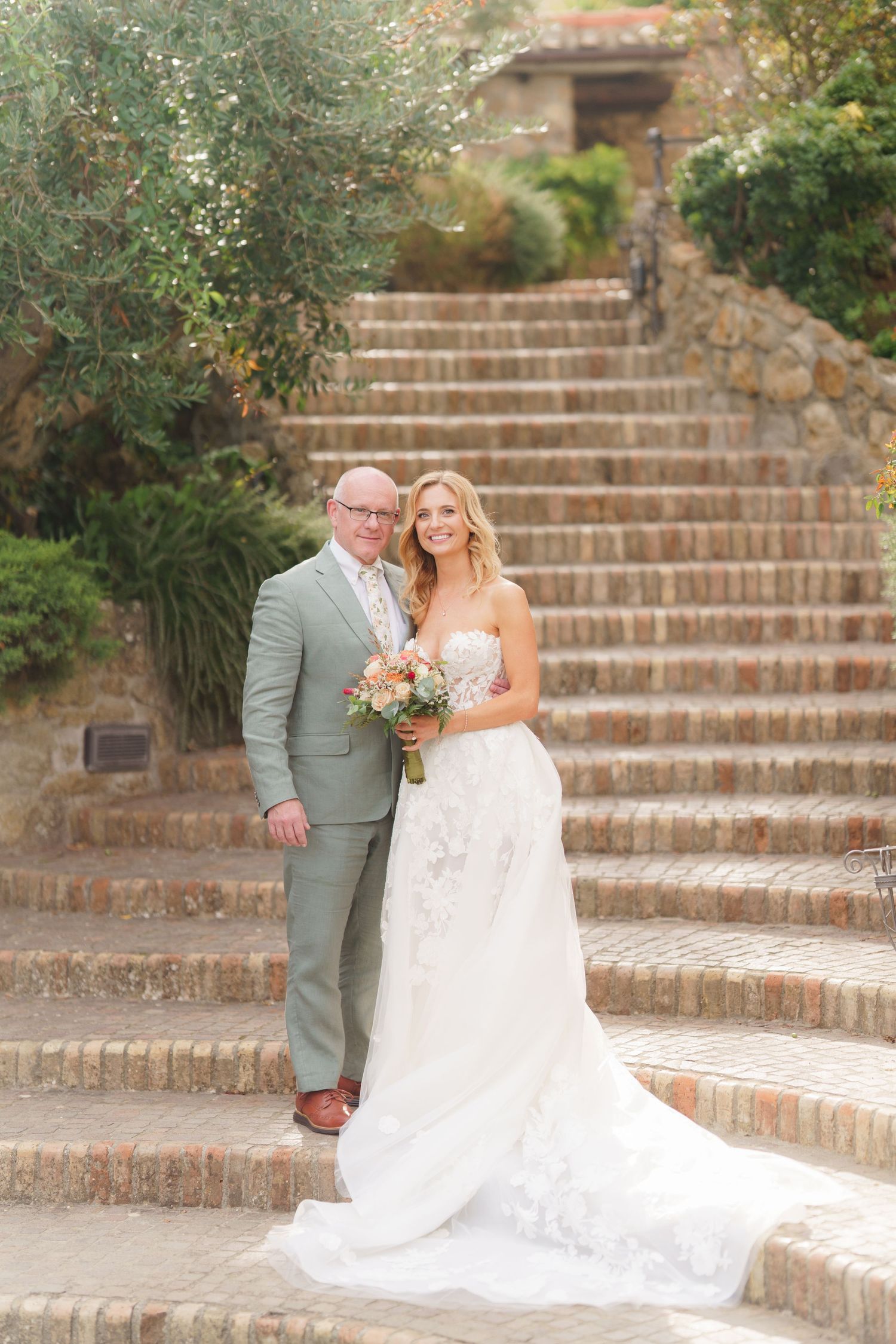 Wedding couple posing on rustic brick stairs surrounded by lush greenery.