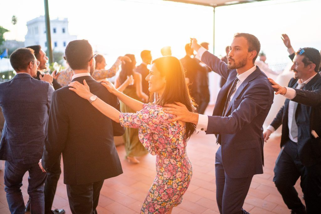 Wedding party dancing in a line at sunset on an outdoor terrace.