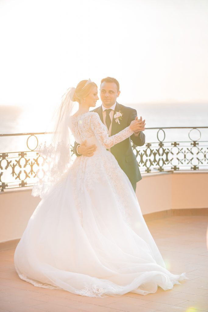 A wedding couple dancing on a terrace overlooking the Mediterranean Sea at golden hour.