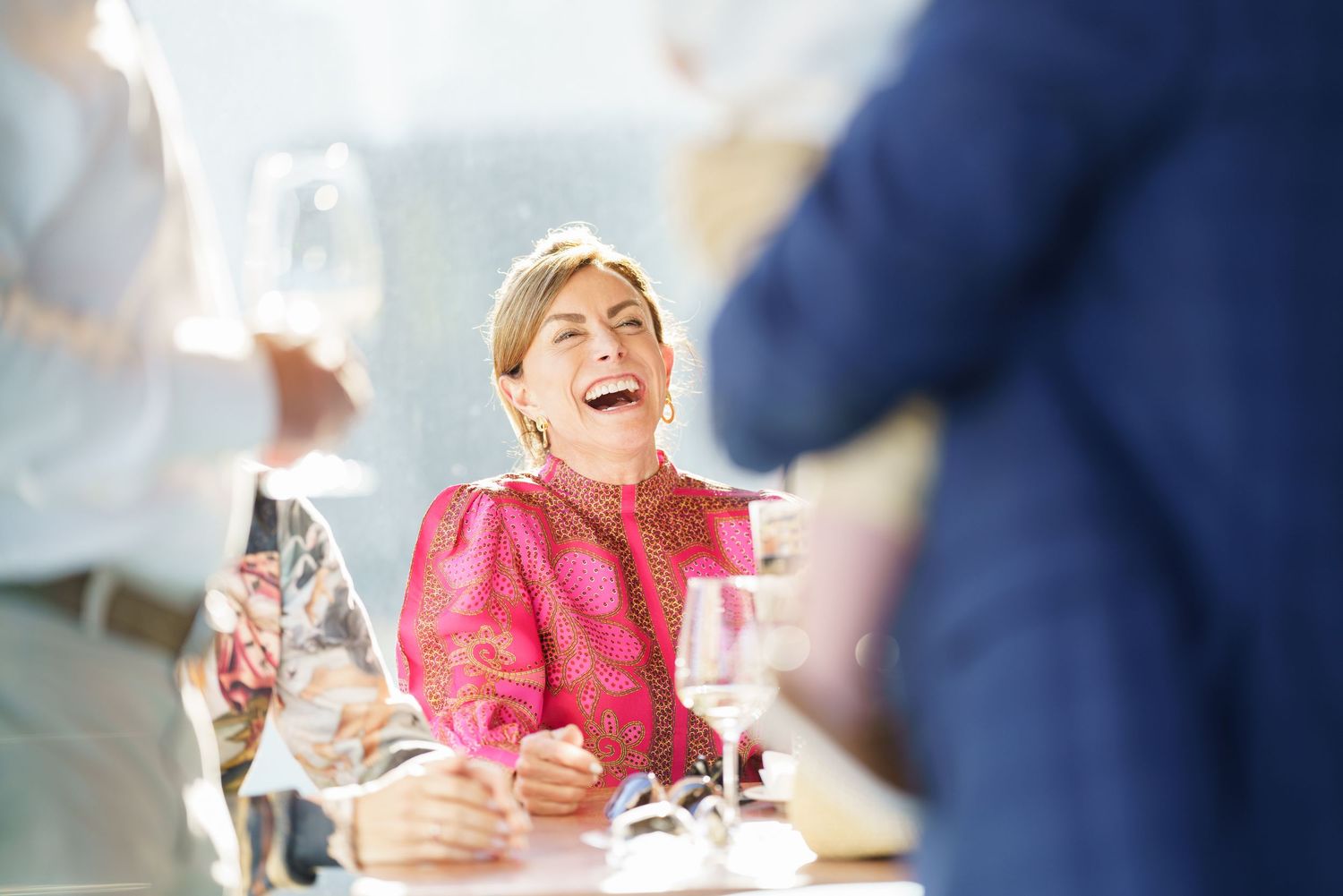 Person in pink dress laughing joyfully during social gathering.