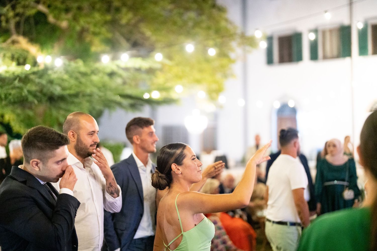 Guests mingle and dance at an elegant outdoor wedding reception under string lights.