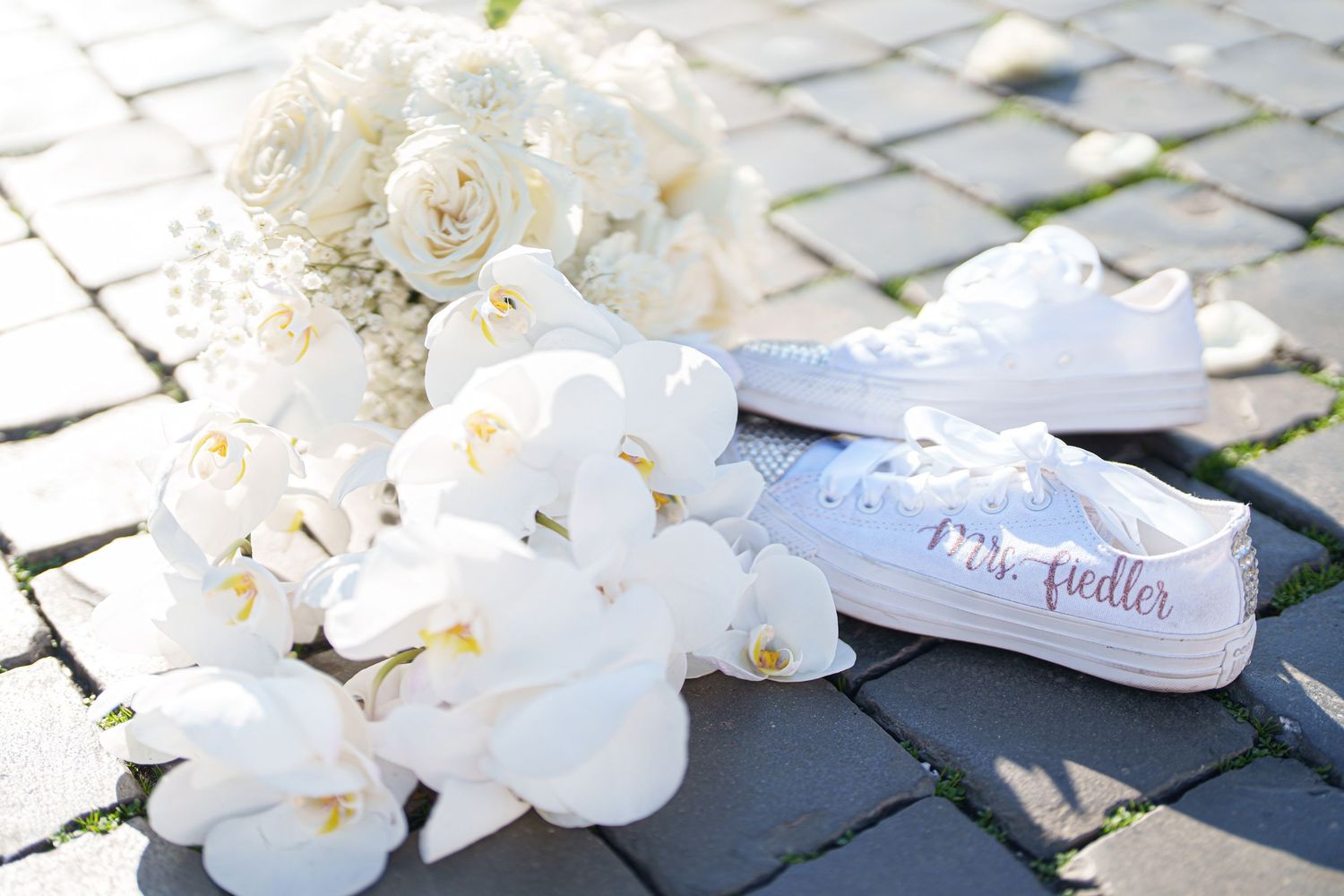 White orchids and custom bridal shoes arranged on stone pavement.