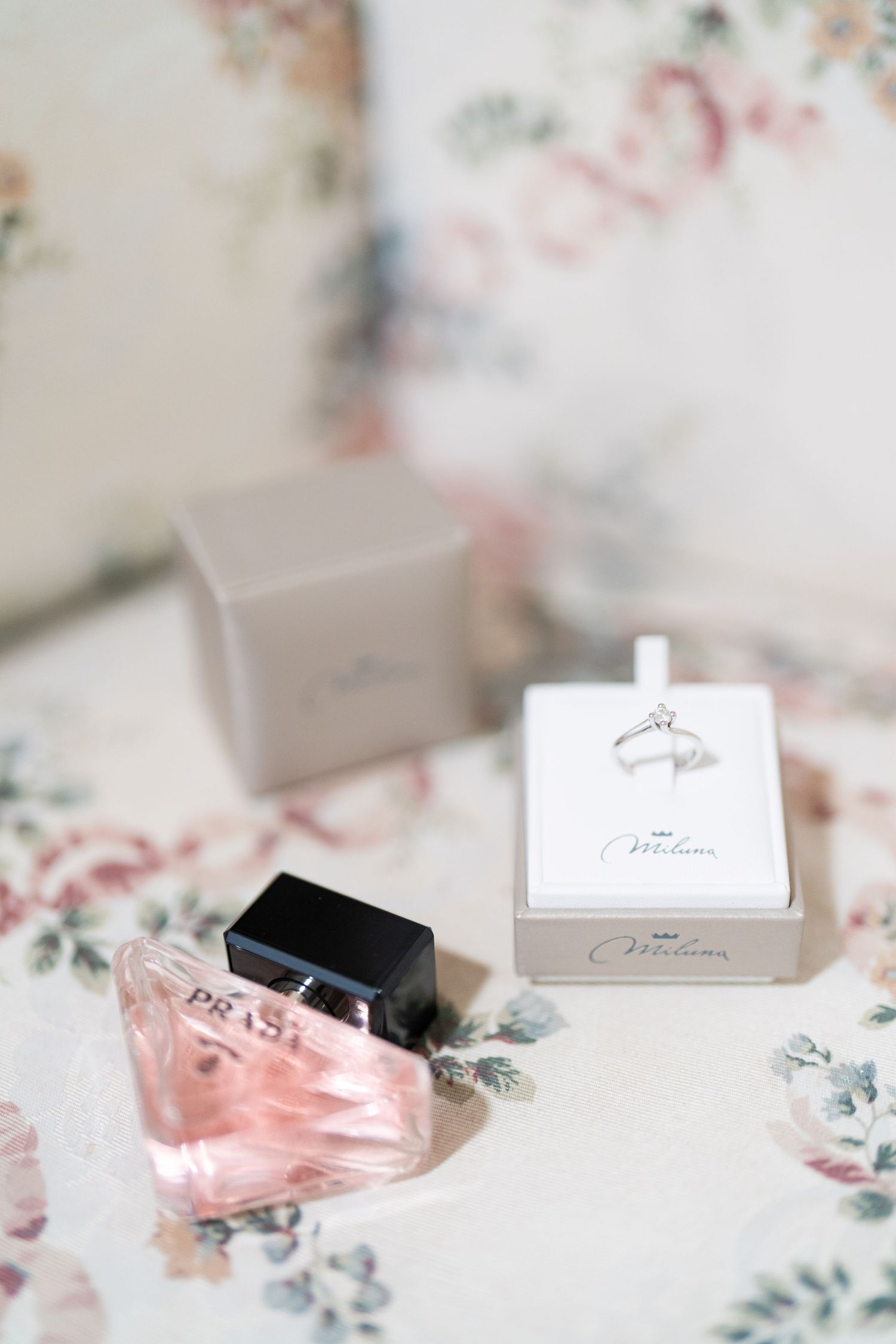 Pink perfume bottle and jewelry boxes arranged on floral patterned surface.