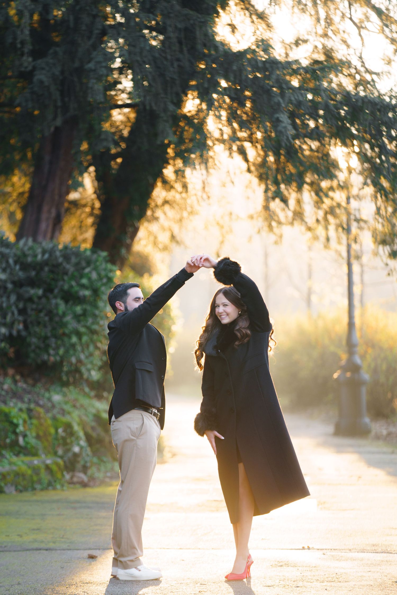 A couple shares a playful moment in a misty park at sunset with golden light filtering through the trees.