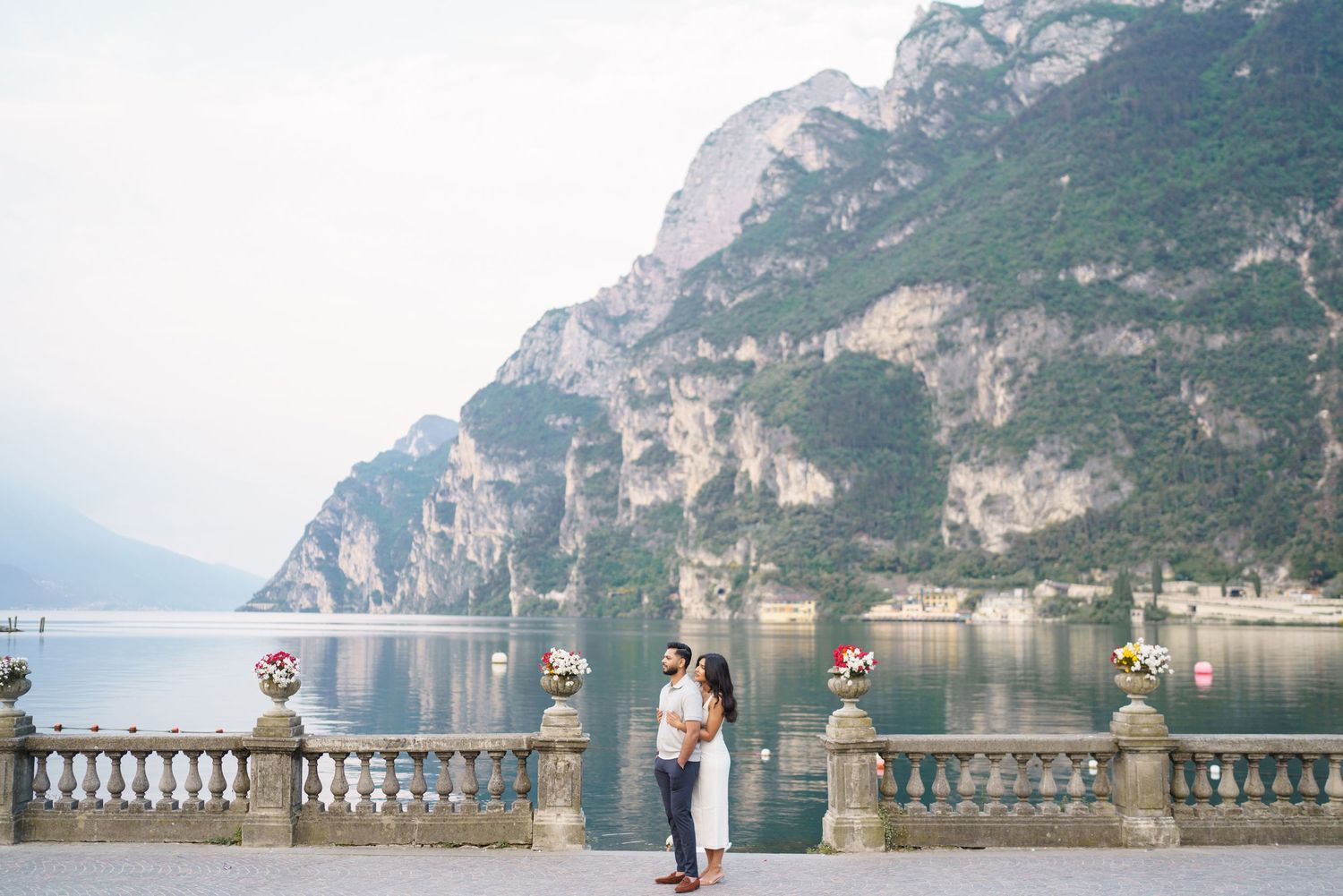 Scenic lakeside terrace with ornate stone balustrade overlooking dramatic mountain cliffs at Lake Garda, Italy.