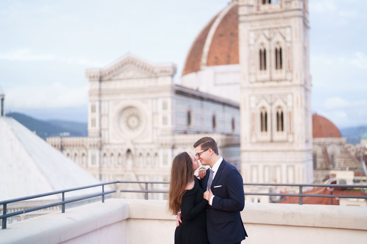 A romantic couple embraces on a balcony overlooking the historic Florence Cathedral and cityscape in Italy.