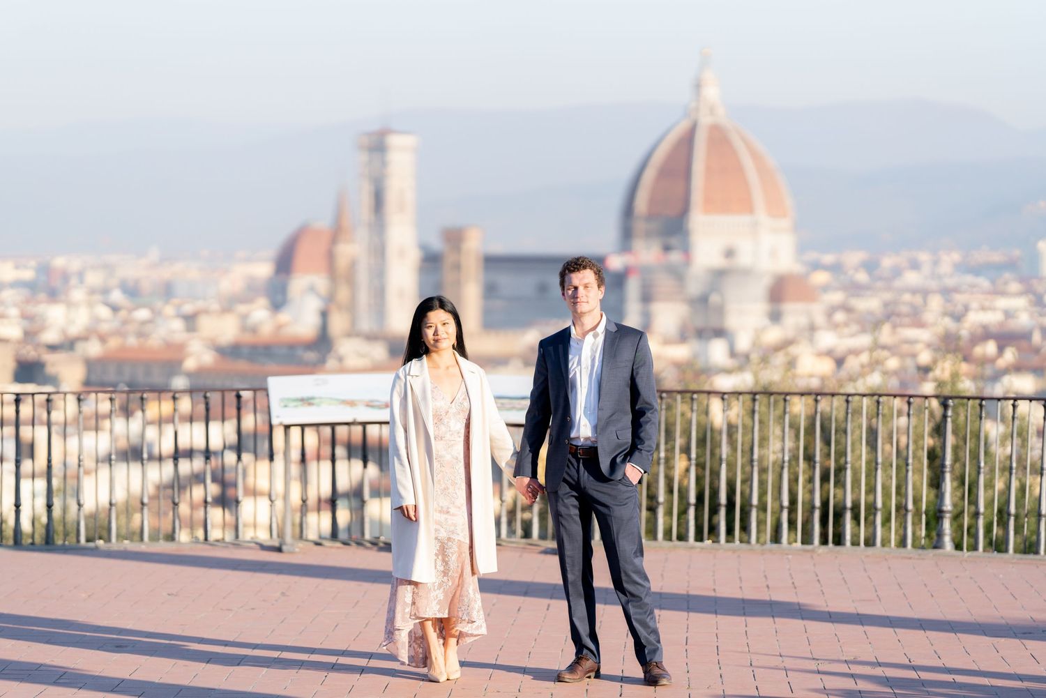 A couple stands at a scenic overlook in Florence, Italy with the Duomo cathedral visible in the city skyline.