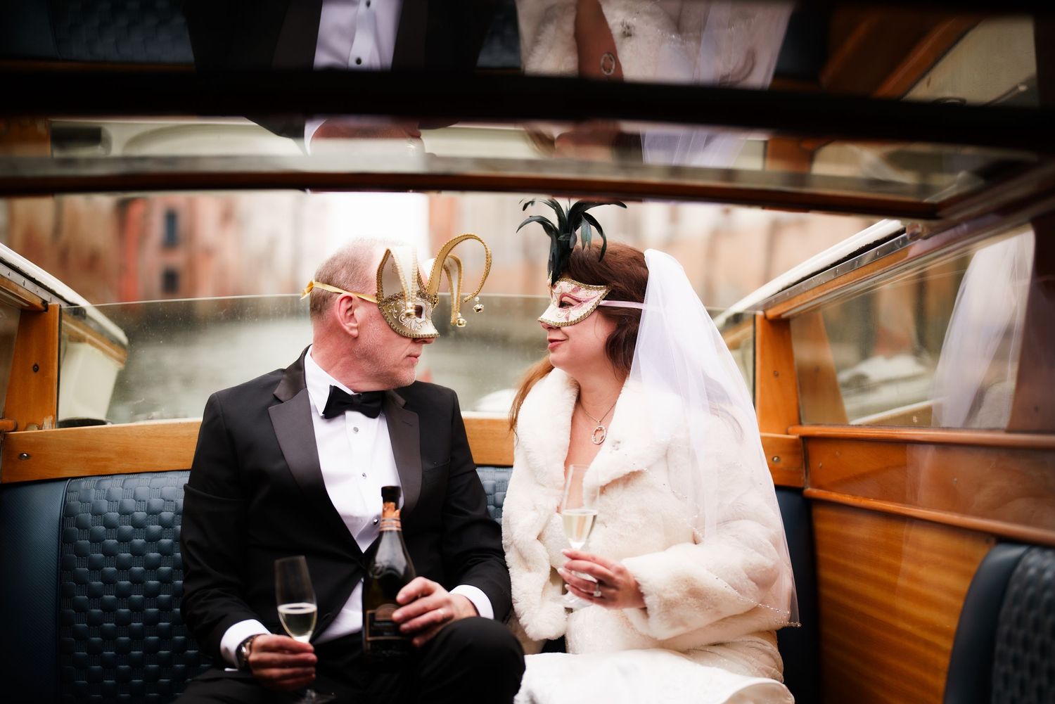 Two people in formal attire share an intimate moment aboard a classic wooden boat during a special occasion.