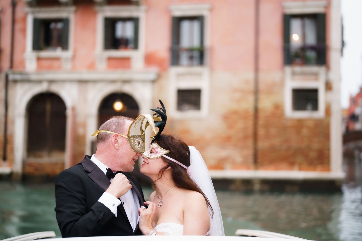 Romantic couple moment captured along Venice canals with pink buildings in background.