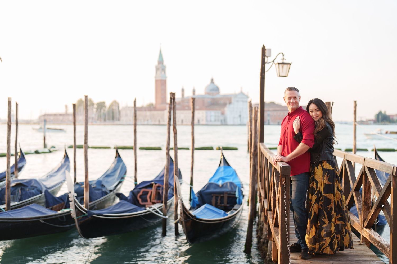 photographer veniceRomantic couple stands on Venice dock with traditional gondolas and San Giorgio Maggiore church in background.