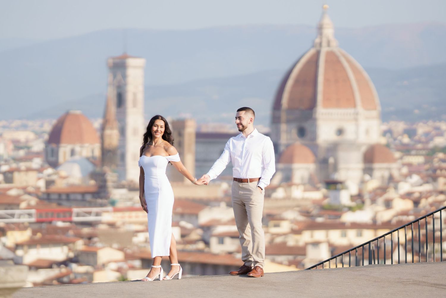 Couple poses on Piazzale Michelangelo overlooking Florence's iconic skyline with the Duomo cathedral at sunset.