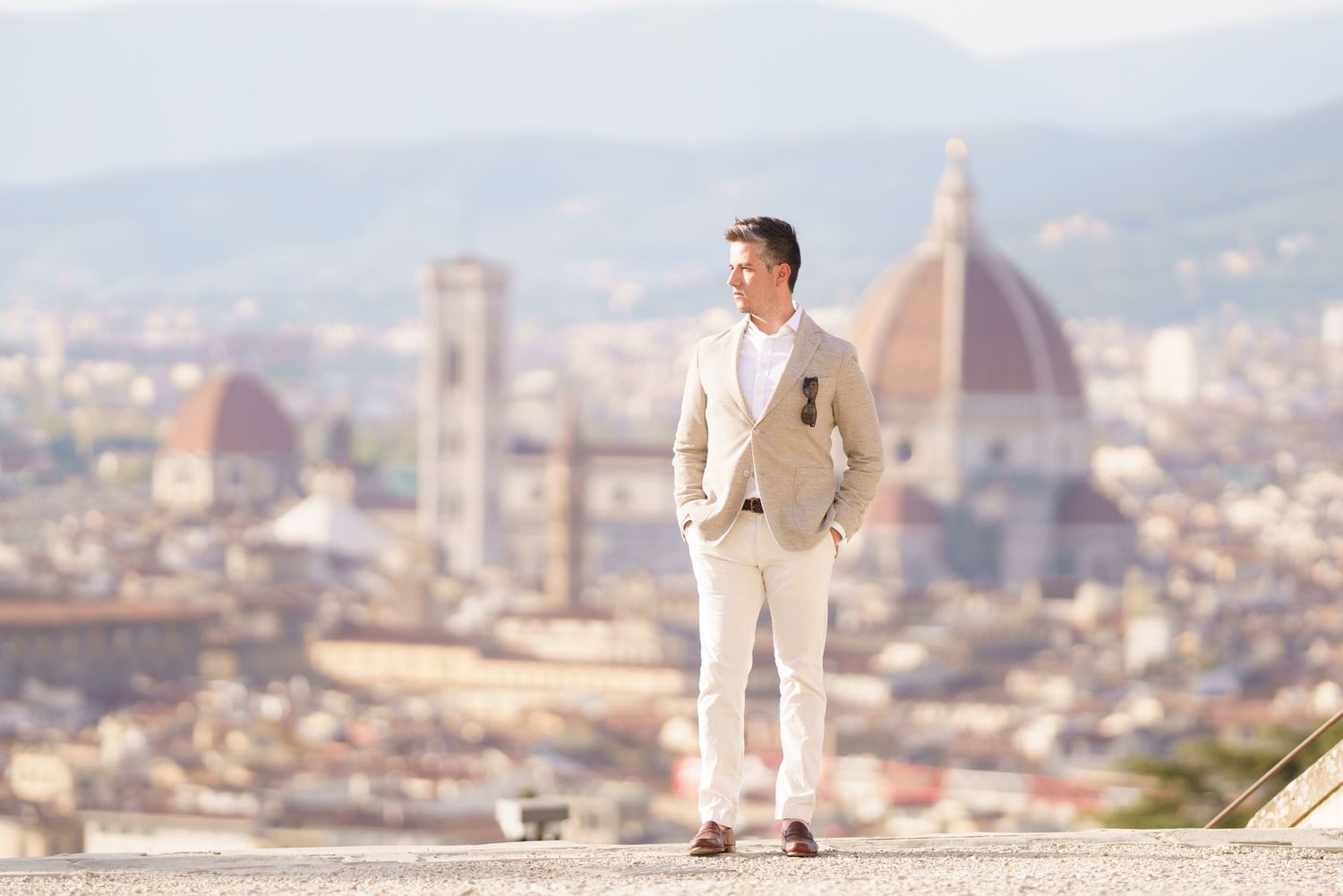 Panoramic view of Florence cityscape with someone posing on a wall overlooking the iconic Duomo cathedral.