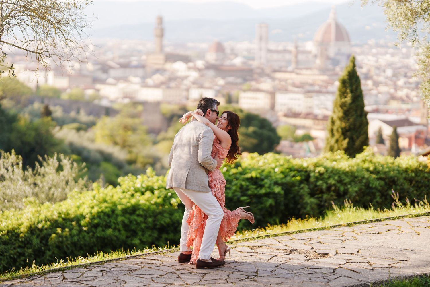 Romantic couple shares tender moment on hilltop overlooking scenic city landscape during golden hour.
