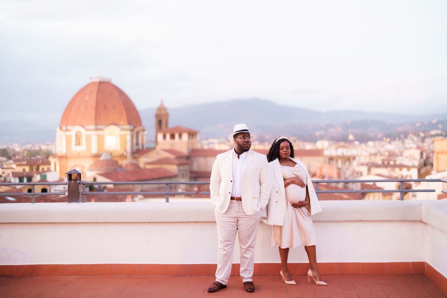 Couple in white attire poses on Florence rooftop with iconic Duomo cathedral dome in background.
