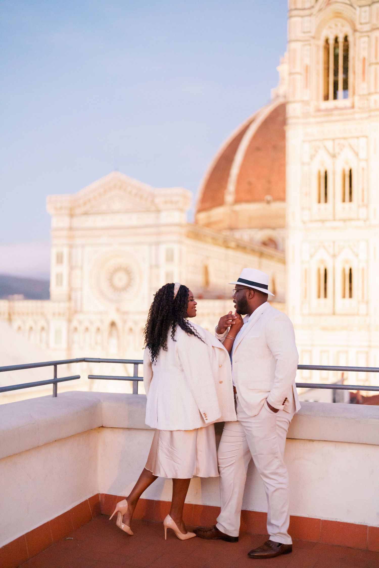 Elegant couple in white attire sharing a romantic moment on a rooftop terrace with Florence Cathedral dome backdrop.