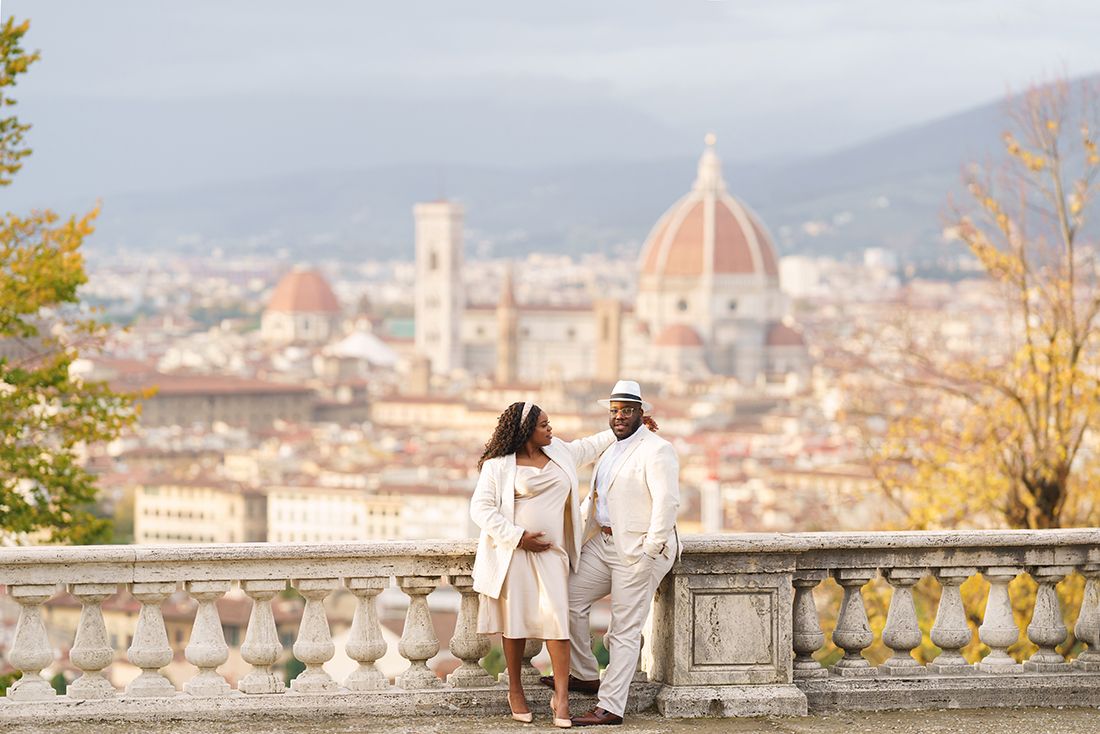 Couple in white outfits posing on a terrace with Florence skyline and Cathedral dome in background.