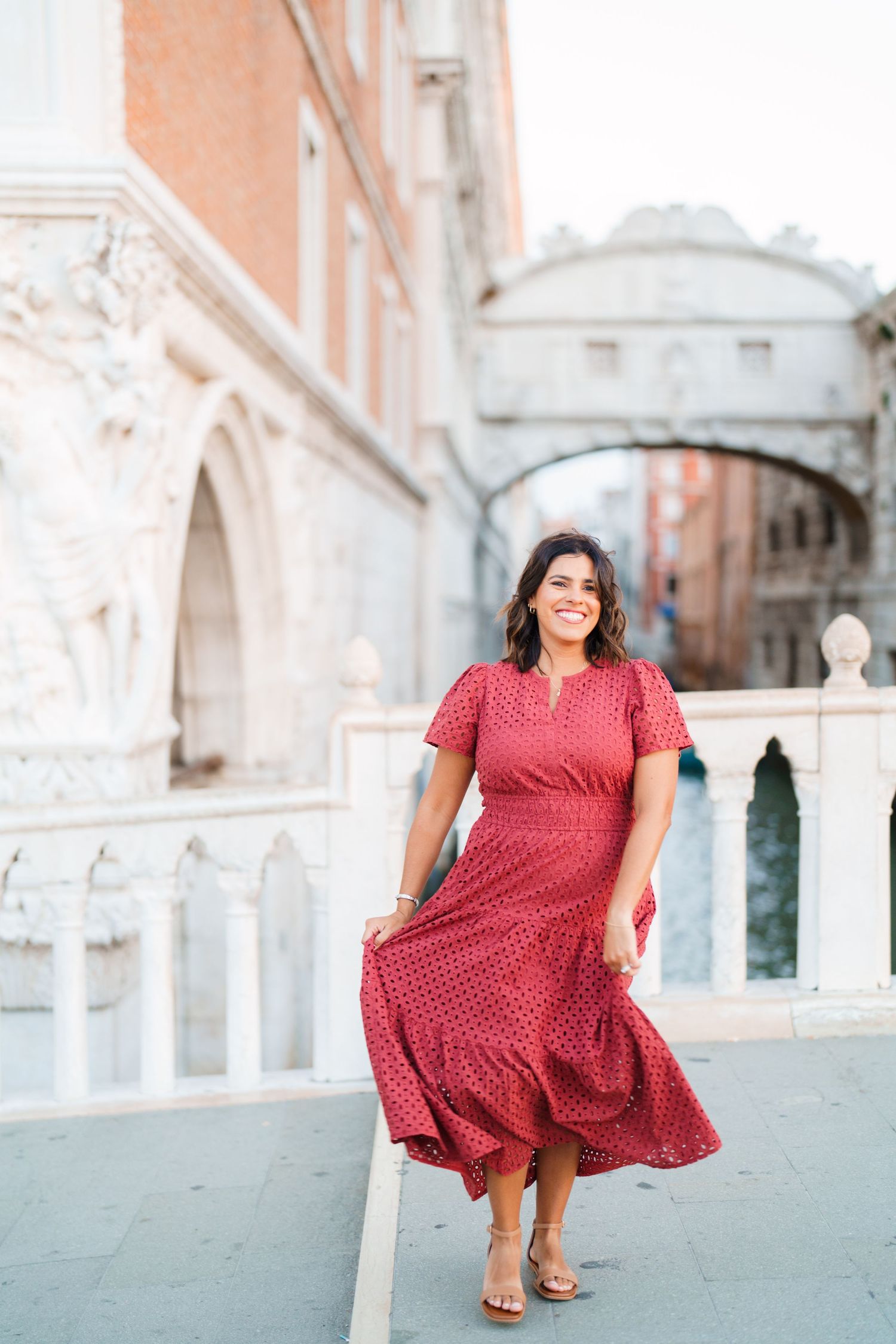 Woman in red midi dress smiling near Bridge of Sighs in Venice, Italy.