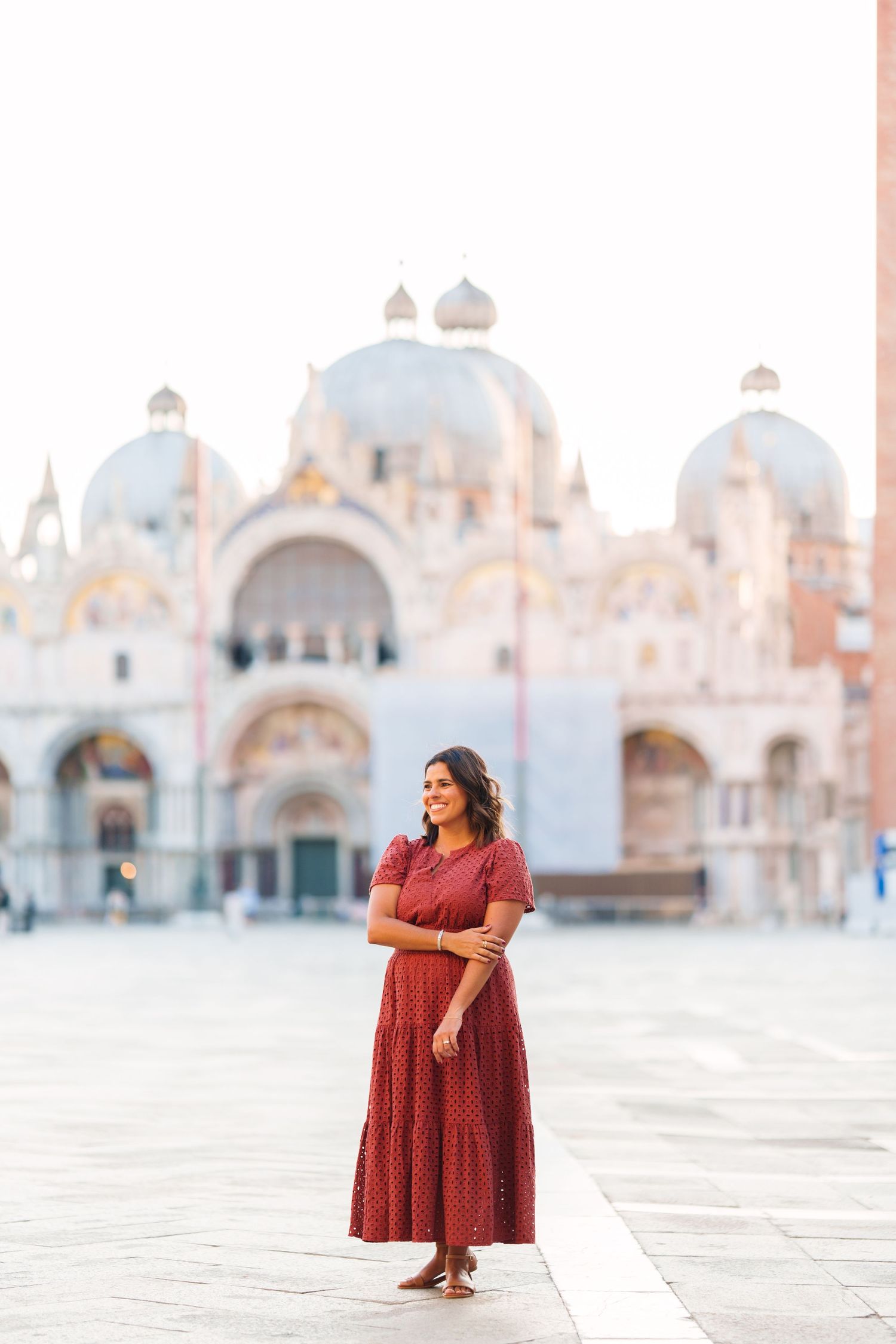 Woman in red dress standing in St. Mark's Square, Venice, with the iconic Basilica di San Marco in the background.