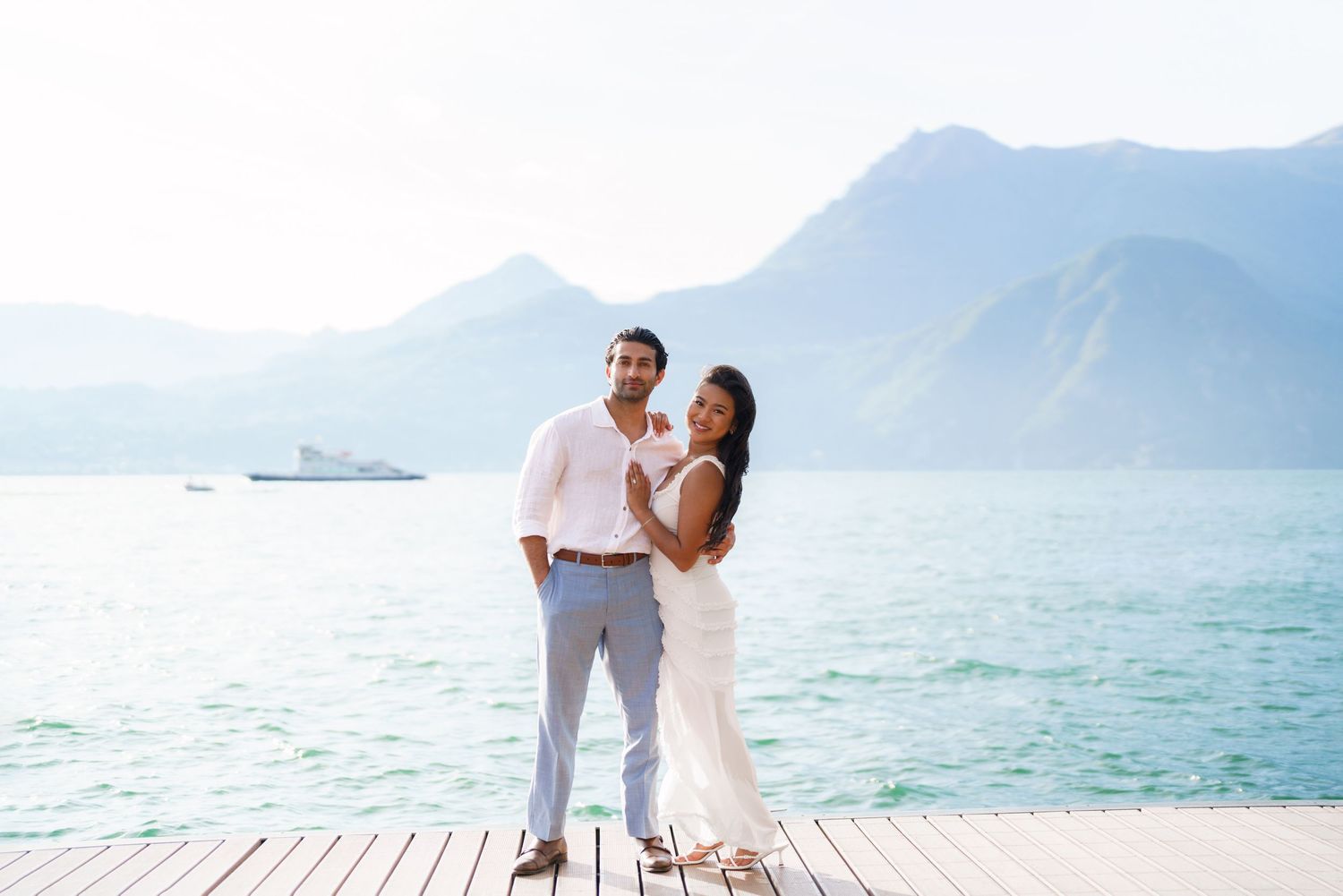 Couple posing on a wooden dock with turquoise lake and mountain backdrop on a sunny day.