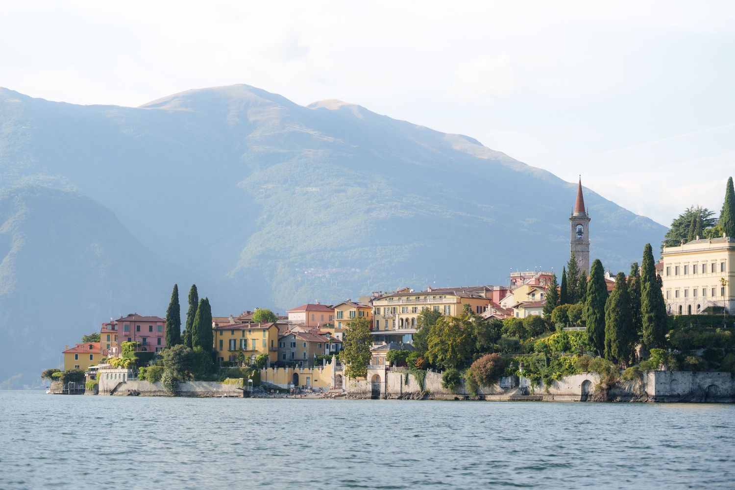 Scenic view of Varenna village on Lake Como with colorful buildings, cypress trees, and mountains in the background.