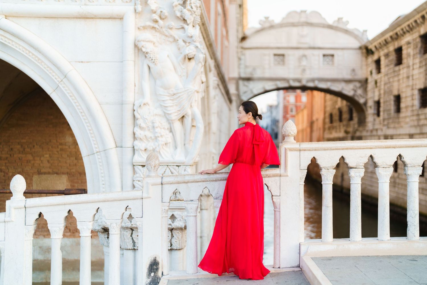 Woman in red gown stands on Venice bridge near Bridge of Sighs, Italy.