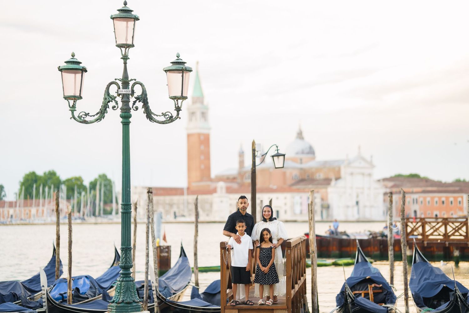 Family posing on a Venice dock with gondolas and San Giorgio Maggiore church in the background.