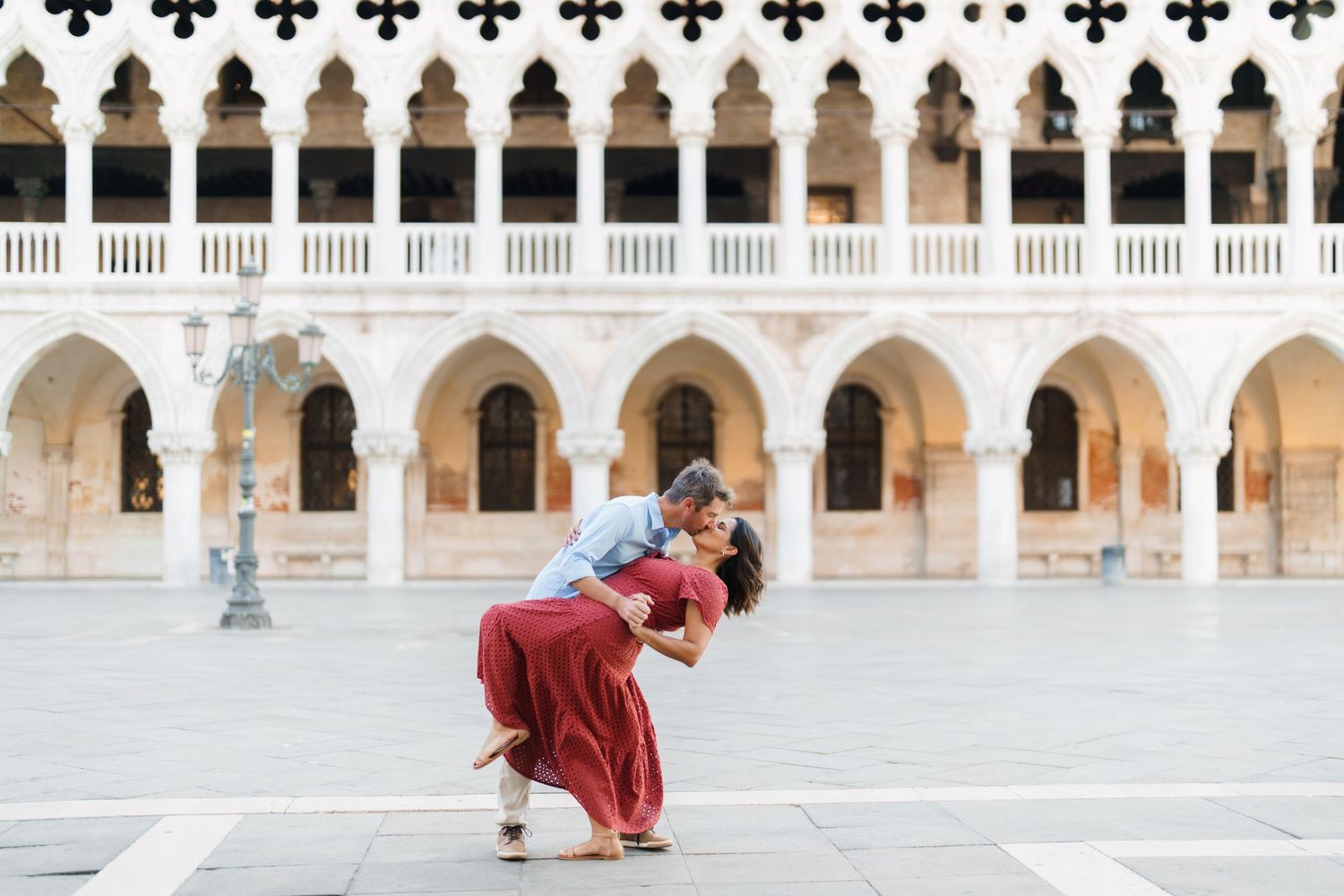 Couple sharing a romantic dip kiss in St. Mark's Square, Venice, with iconic Gothic arches in the background.