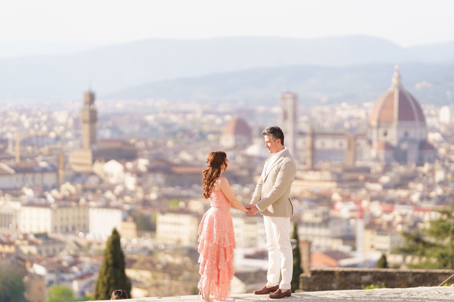 A romantic couple admires the stunning panoramic view of Florence, Italy with its iconic Duomo cathedral in the distance.