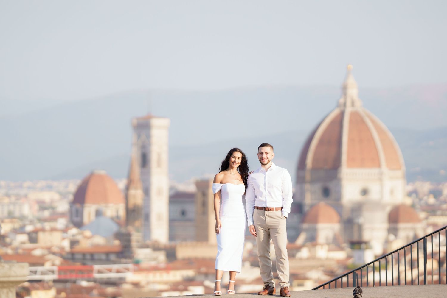 A couple poses on Piazzale Michelangelo overlooking the Florence cityscape with Duomo cathedral in background.