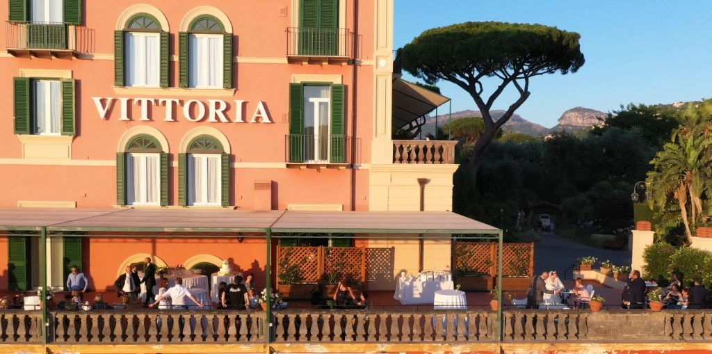 Panoramic view of a luxury Italian hotel with terracotta walls and arched windows overlooking the Mediterranean Sea.