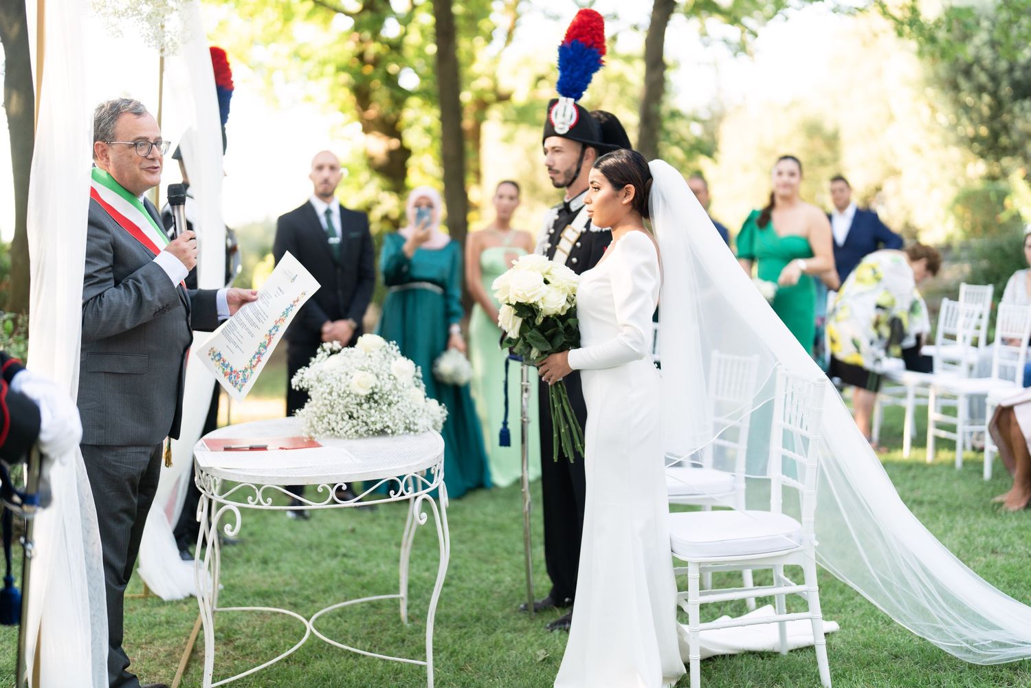 Outdoor wedding ceremony setup with white chairs and floral arrangements along a garden path.