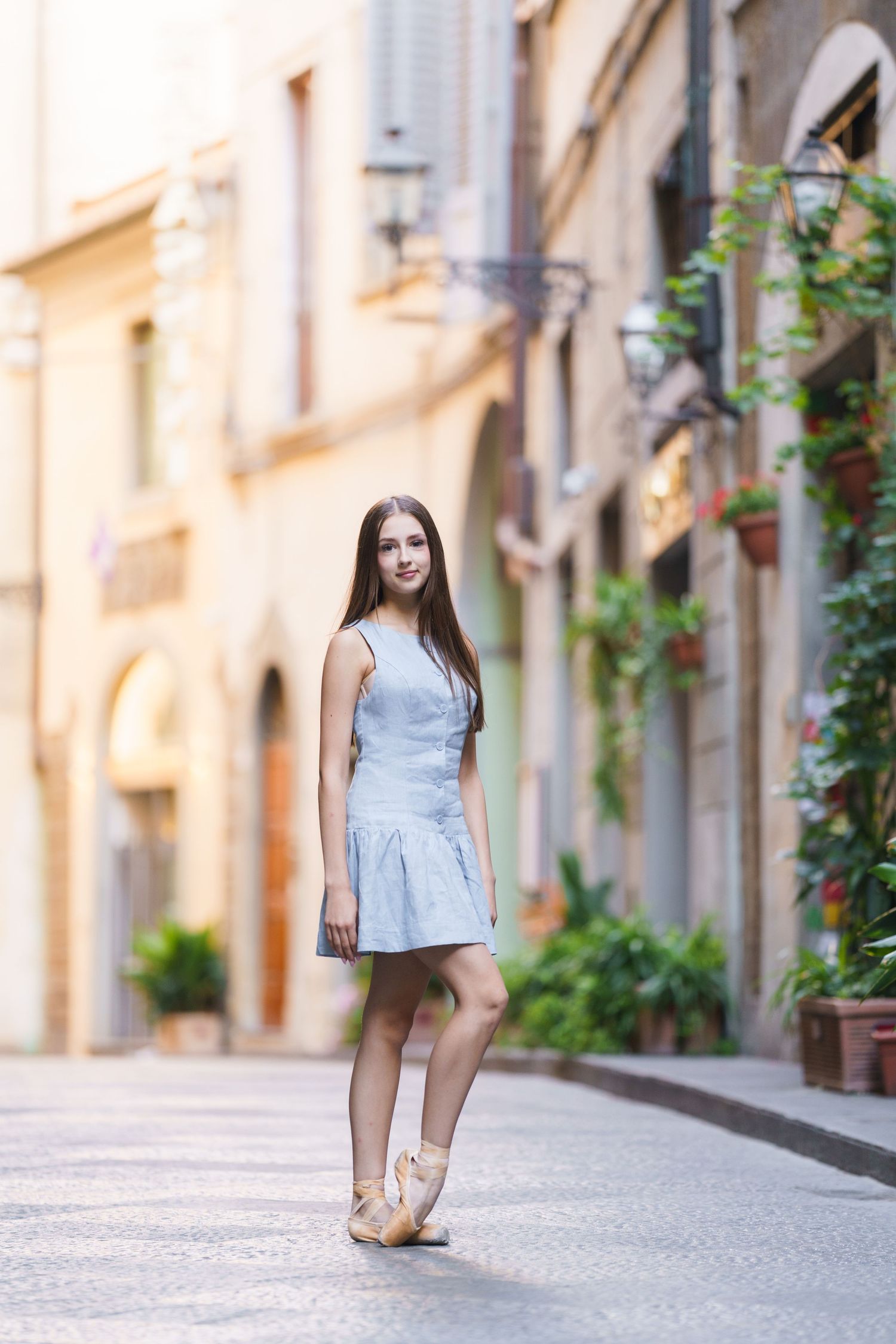 A person in a light blue dress walks along a charming European cobblestone street lined with historic buildings.