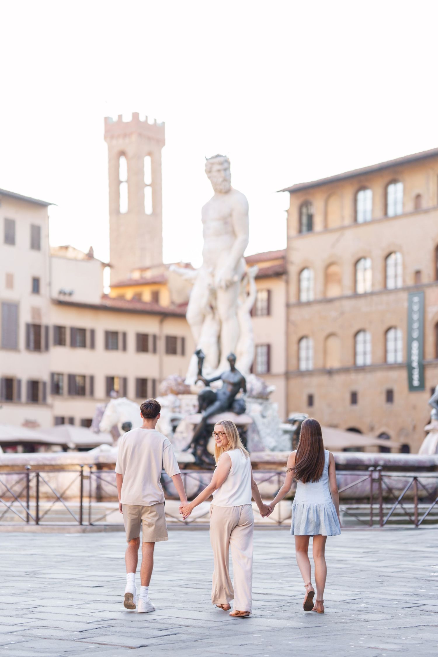 Tourists walk through Piazza della Signoria in Florence, Italy with the Neptune Fountain and historic architecture visible.