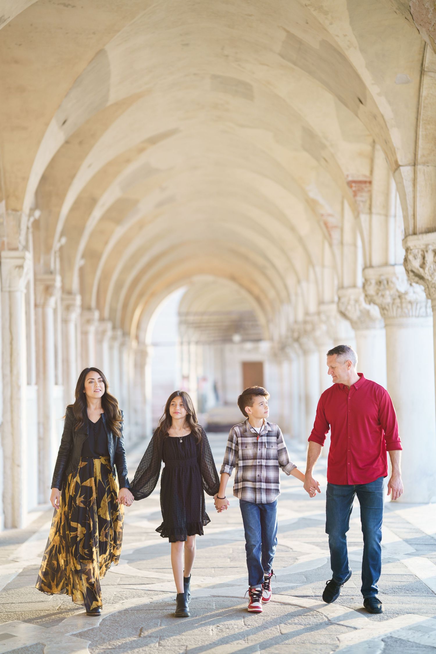 People walking through an elegant arched colonnade with sunlight casting dramatic shadows on the ground.