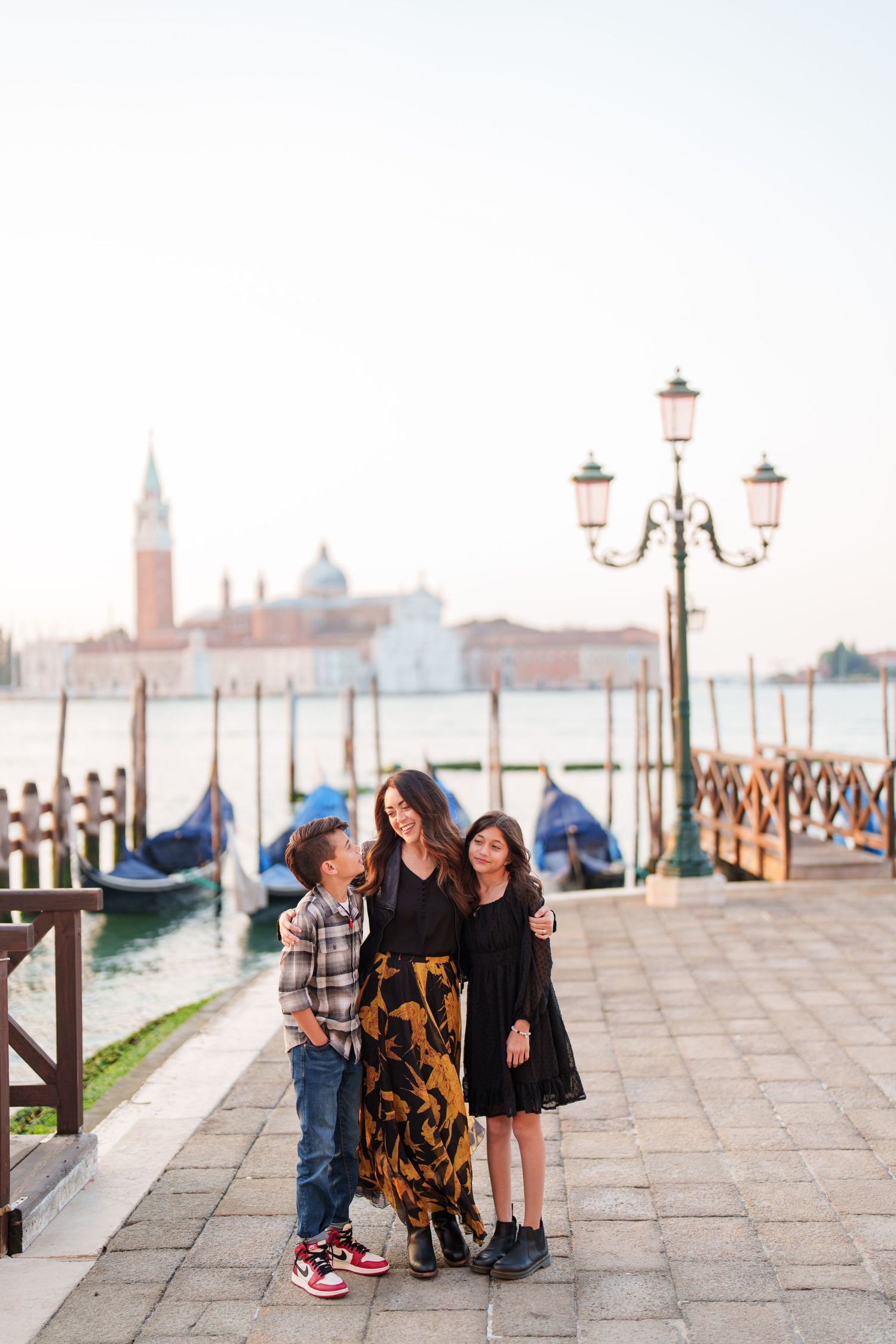 Family enjoying a moment together on a stone walkway along Venice's waterfront with historic buildings in the background.