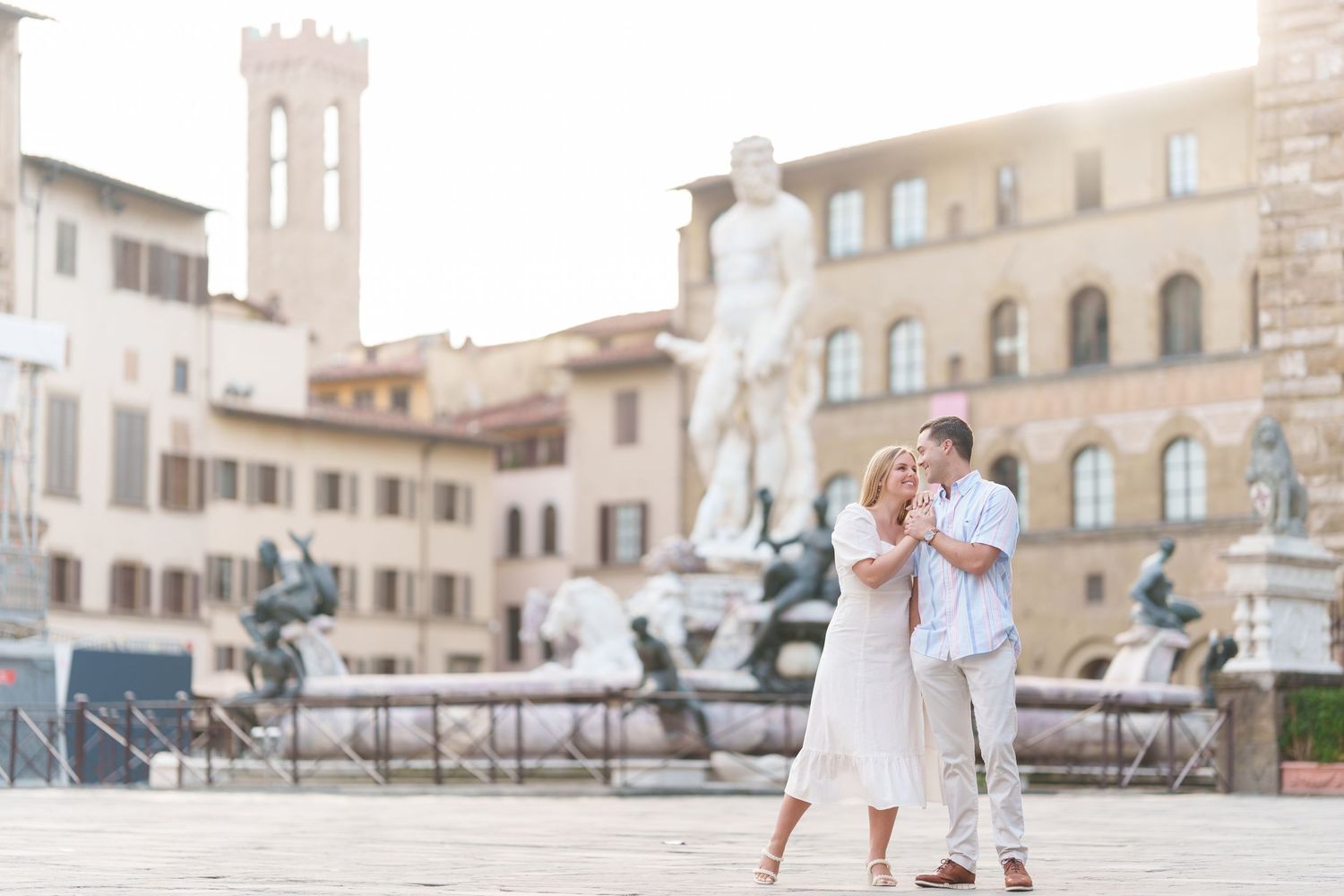A couple embraces in Florence's Piazza della Signoria with historic architecture and statues in the background.