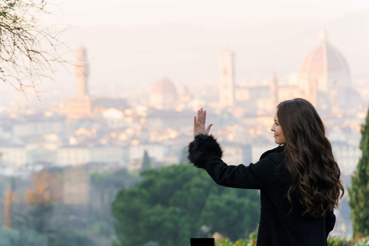 A silhouetted figure waves while overlooking the historic skyline of Florence, Italy during a misty sunset.
