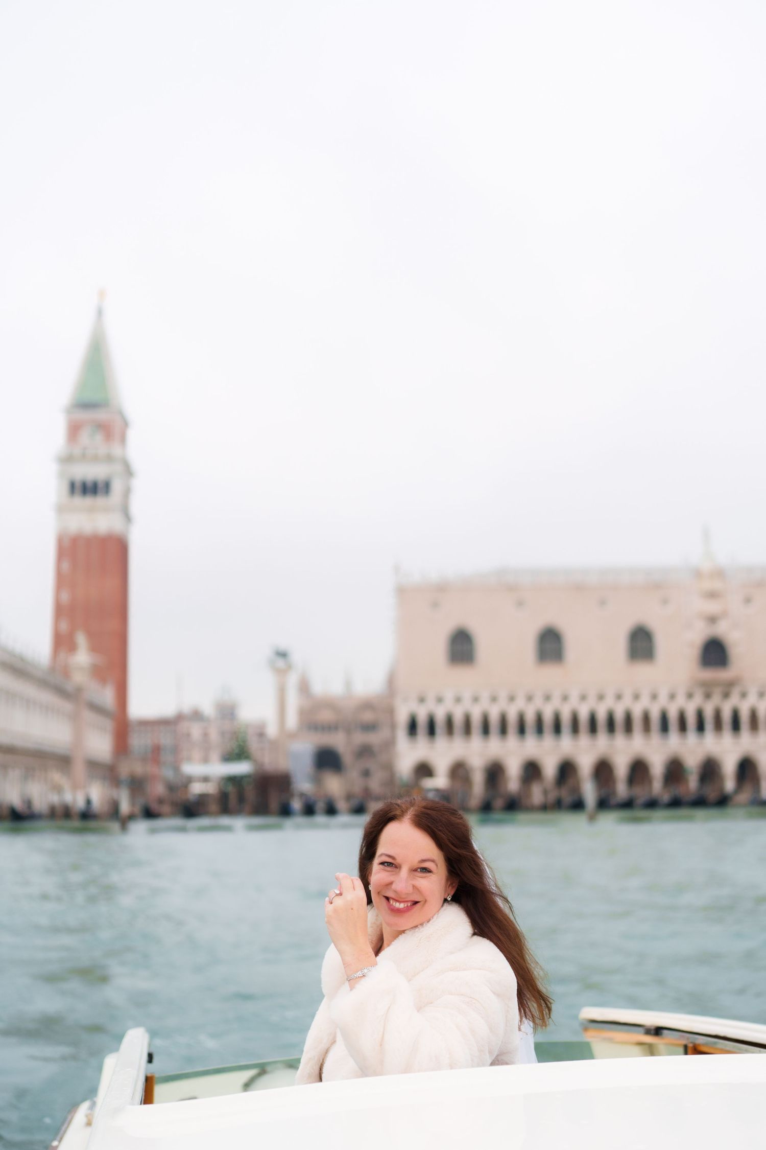 Tourist on boat in Venice with iconic St Mark's Campanile and Doge's Palace in background on cloudy day.