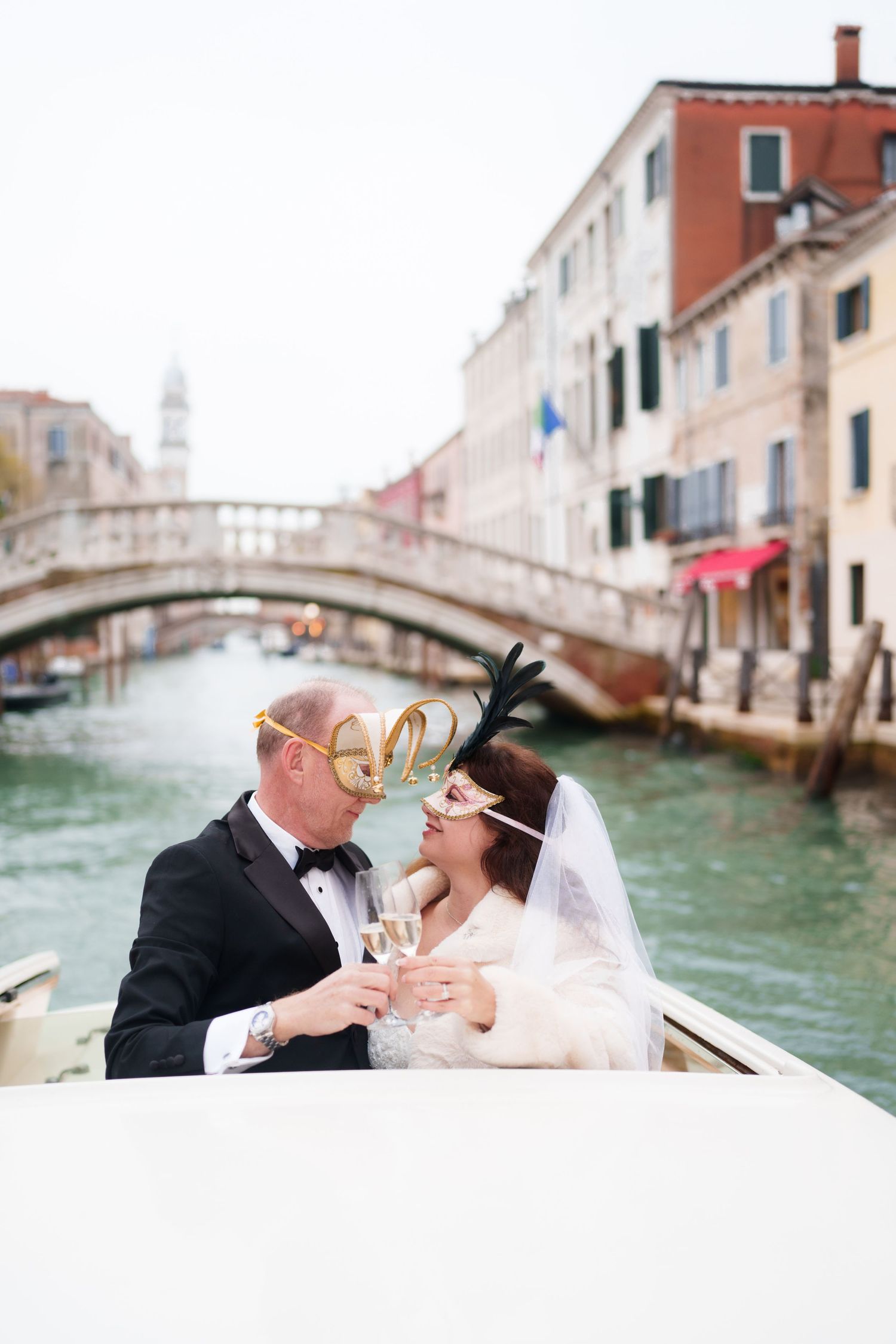 A romantic wedding scene in Venice with a couple in a gondola and historic bridge in the background.
